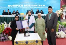 Seorang dokter baru wanita FK Unimus mengenakan jas putih memegang map dokumen sumpah didampingi orang tua dan pimpinan fakultas di atas panggung Sumpah Dokter XLV.