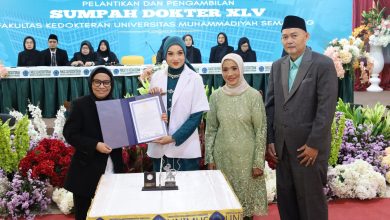 Seorang dokter baru wanita FK Unimus mengenakan jas putih memegang map dokumen sumpah didampingi orang tua dan pimpinan fakultas di atas panggung Sumpah Dokter XLV.