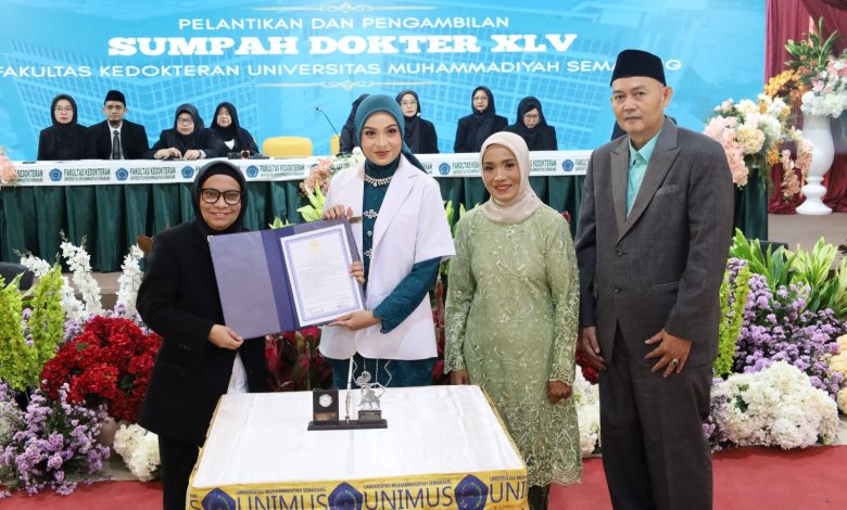 Seorang dokter baru wanita FK Unimus mengenakan jas putih memegang map dokumen sumpah didampingi orang tua dan pimpinan fakultas di atas panggung Sumpah Dokter XLV.