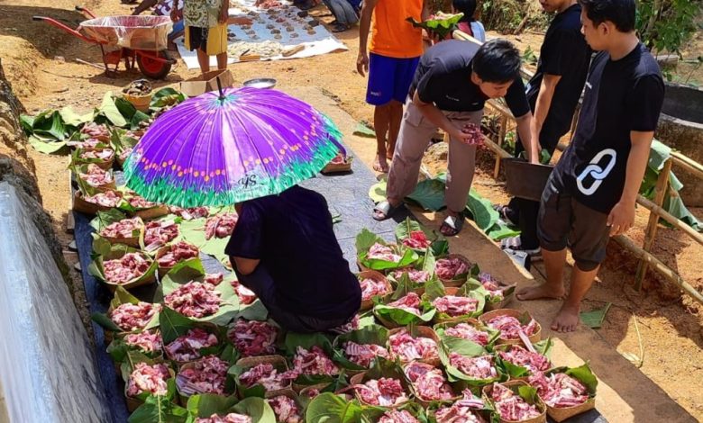 Grid keranjang anyaman hijau berisi daging qurban merah mentah yang tertata rapi di atas terpal, di bawah pengawasan sukarelawan dengan payung ungu di lokasi luar ruangan.