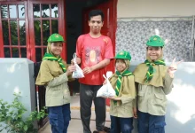 Tiga siswa pramuka Hizbul Wathan MIM Kauman memberikan kantong plastik putih berisi paket bantuan daging kurban dan beras kepada seorang warga pria di depan pintu merah rumahnya, dalam kegiatan PERBAQU XIII.