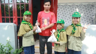 Tiga siswa pramuka Hizbul Wathan MIM Kauman memberikan kantong plastik putih berisi paket bantuan daging kurban dan beras kepada seorang warga pria di depan pintu merah rumahnya, dalam kegiatan PERBAQU XIII.