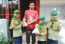 Tiga siswa pramuka Hizbul Wathan MIM Kauman memberikan kantong plastik putih berisi paket bantuan daging kurban dan beras kepada seorang warga pria di depan pintu merah rumahnya, dalam kegiatan PERBAQU XIII.