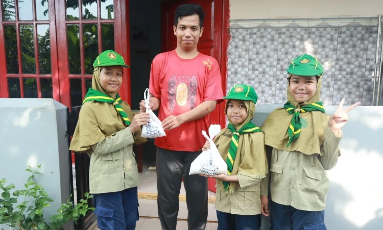 Tiga siswa pramuka Hizbul Wathan MIM Kauman memberikan kantong plastik putih berisi paket bantuan daging kurban dan beras kepada seorang warga pria di depan pintu merah rumahnya, dalam kegiatan PERBAQU XIII.