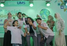 Sekelompok mahasiswa Universitas Muhammadiyah Surakarta (UMS) berswafoto bersama dengan tongkat selfie gimbal di atas panggung dengan spanduk "The 9th Social Gathering of ENGLISH TUTORIAL PROGRAM" dan logo perdamaian, di bawah pencahayaan panggung hijau. Foto ini menangkap kegembiraan dan ekspresi perdamaian global melalui kreativitas mahasiswa.