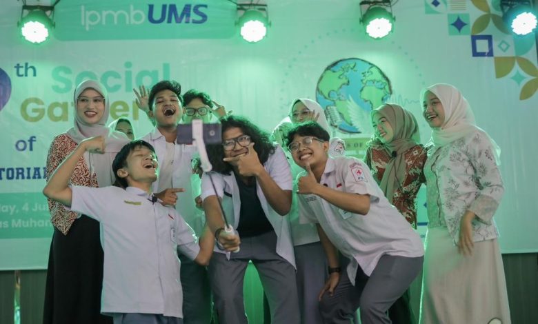 Sekelompok mahasiswa Universitas Muhammadiyah Surakarta (UMS) berswafoto bersama dengan tongkat selfie gimbal di atas panggung dengan spanduk "The 9th Social Gathering of ENGLISH TUTORIAL PROGRAM" dan logo perdamaian, di bawah pencahayaan panggung hijau. Foto ini menangkap kegembiraan dan ekspresi perdamaian global melalui kreativitas mahasiswa.