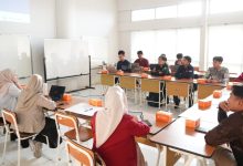 Sekelompok orang duduk di ruang kelas mendengarkan presentasi