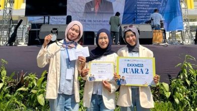Tiga mahasiswi UMPWR berhijab dan mengenakan almamater krem, tersenyum bangga memegang medali dan sertifikat "Juara 2" di ajang EKKN 4 Universitas Tidar. Mereka berpose di depan panggung acara outdoor.
