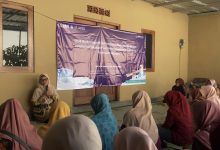 Sekelompok wanita duduk di lantai mendengarkan ceramah di ruangan dengan spanduk PKM UMS ungu besar di latar belakang.