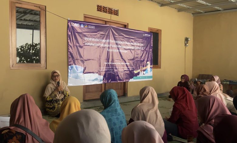 Sekelompok wanita duduk di lantai mendengarkan ceramah di ruangan dengan spanduk PKM UMS ungu besar di latar belakang.