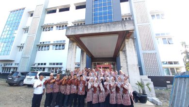 Foto bersama puluhan guru dan karyawan MI Muhammadiyah Danurejo Temanggung berbaju batik cokelat seragam dengan jajaran MI Muhammadiyah Ajibarang di depan gedung madrasah megah berlantai tiga dengan fasad biru abu-abu.