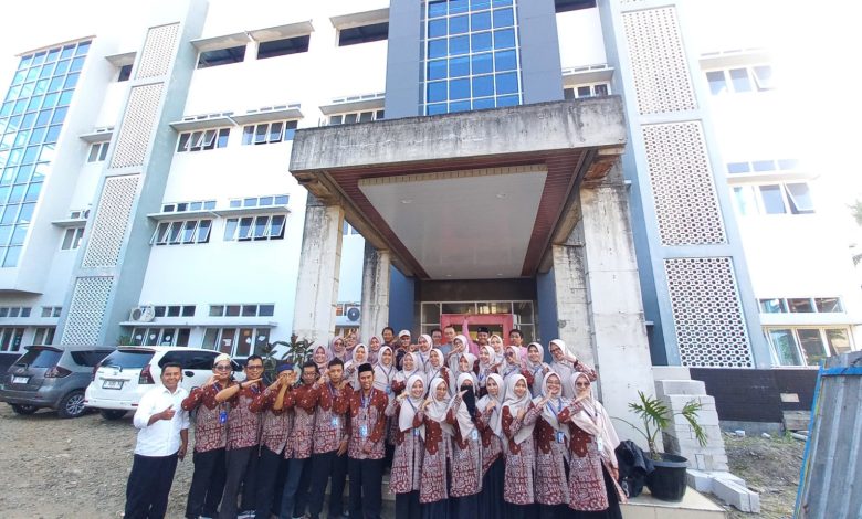 Foto bersama puluhan guru dan karyawan MI Muhammadiyah Danurejo Temanggung berbaju batik cokelat seragam dengan jajaran MI Muhammadiyah Ajibarang di depan gedung madrasah megah berlantai tiga dengan fasad biru abu-abu.