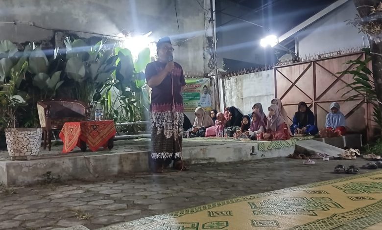 Ustaz Dwi Jatmiko berceramah menggunakan mikrofon di panggung terbuka Teras Beramal Kerten Solo pada malam hari dihadiri jamaah ibu-ibu dan anak-anak yang duduk lesehan dalam Pengajian Arloji.