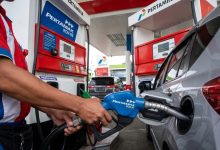 Petugas SPBU Pertamina berbaju merah kombinasi biru sedang memasukkan nosel biru Pertamax RON 92 ke dalam tangki bensin mobil pribadi berwarna perak.