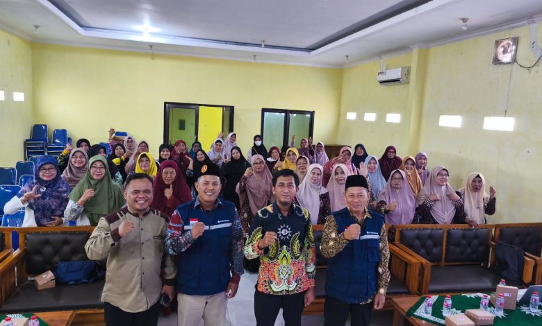 Empat orang pimpinan pria berdiri mengepalkan tangan di depan puluhan jemaah perempuan berhijab yang duduk rapi dalam sebuah ruang pertemuan atau aula berdidinding kuning.