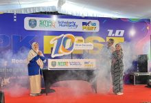 Tiga orang guru dan pimpinan sekolah berdiri bertepuk tangan di atas panggung dengan efek asap dalam acara perayaan satu dekade SMA Muhammadiyah PK Kottabarat Surakarta.