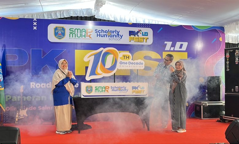 Tiga orang guru dan pimpinan sekolah berdiri bertepuk tangan di atas panggung dengan efek asap dalam acara perayaan satu dekade SMA Muhammadiyah PK Kottabarat Surakarta.