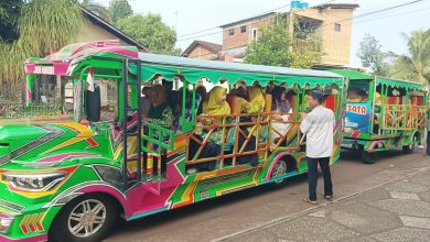Jamaah wanita Muhammadiyah dan Aisyiyah Jepara berkerudung hijau dan kuning duduk di dalam kereta wisata hijau terintegrasi untuk berangkat pengajian.