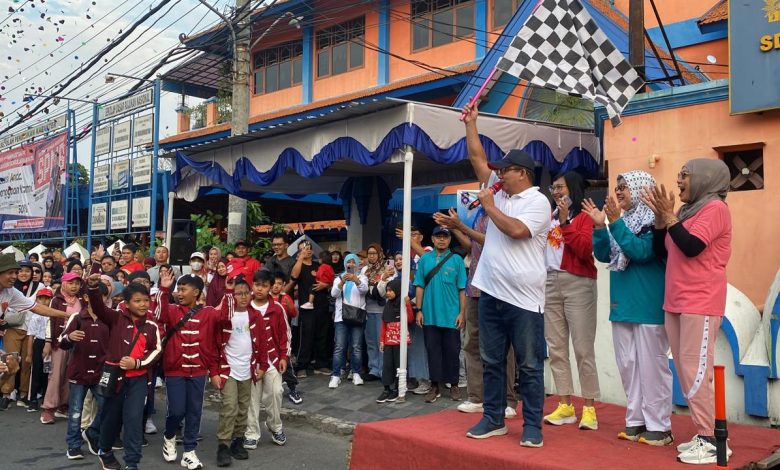 Sekretaris Dinas Pendidikan Kota Surakarta Tarno mengangkat bendera start hitam-putih di panggung didampingi panitia saat melepas peserta Jalan Sehat Keluarga dalam acara Family Day SD Muhammadiyah 1 Solo.