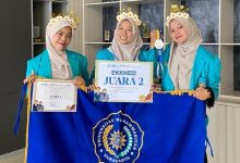 Tiga mahasiswa PG-PAUD UMS tersenyum memakai jas almamater biru sembari memegang sertifikat, medali, dan papan penghargaan Juara 2 EKKN 4 tahun 2026, di depannya terbentang bendera biru Universitas Muhammadiyah Surakarta.