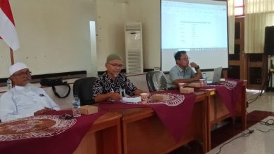 Suasana sidang pleno reorganisasi pengurus HW Drumband Cilacap periode 2025-2028 di gedung BLK-I Cilacap, menampilkan tiga orang pengurus di meja pimpinan dan layar proyektor susunan pengurus.