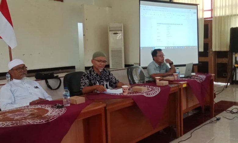 Suasana sidang pleno reorganisasi pengurus HW Drumband Cilacap periode 2025-2028 di gedung BLK-I Cilacap, menampilkan tiga orang pengurus di meja pimpinan dan layar proyektor susunan pengurus.