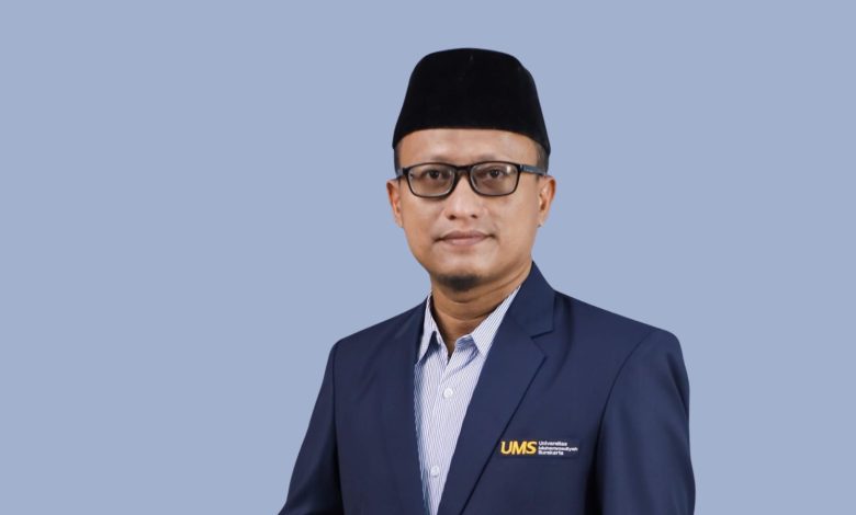 Foto profil Dr. Ainur Rha’in, S.Th.I., M.Th.I., Dosen FAI UMS, mengenakan jas biru UMS dan peci hitam, tersenyum ramah dengan latar belakang abu-abu lavender.