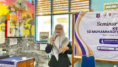 Seorang pembicara wanita berhijab sedang berbicara di depan peserta seminar parenting SD Muhammadiyah dengan spanduk acara di latar belakang.