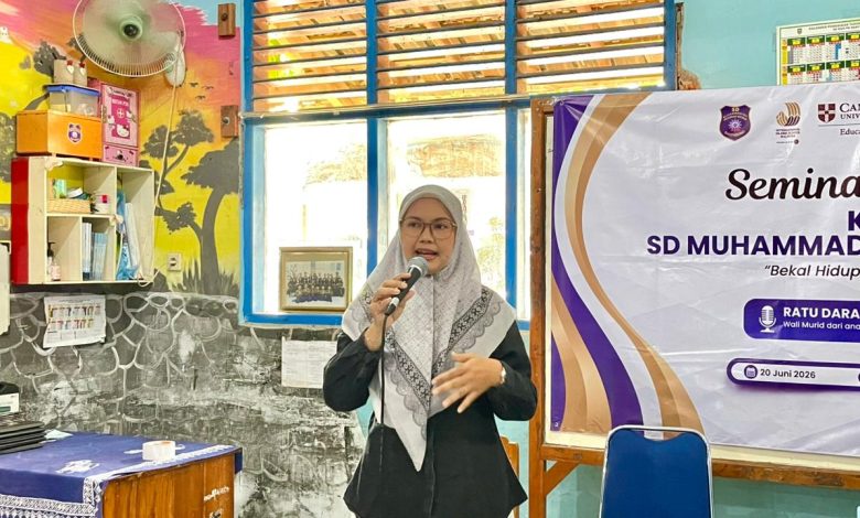Seorang pembicara wanita berhijab sedang berbicara di depan peserta seminar parenting SD Muhammadiyah dengan spanduk acara di latar belakang.