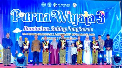 Foto bersama siswa berprestasi berselempang dengan kepala sekolah, Kadinas P dan K Kota Magelang Nurwiyono, SN, M. Pd, Pimpinan Daerah Muhammadiyah, pengawas, dan dewan pendidikan di atas panggung acara Wisuda Purna Wiyata 3 SD Mutual Dua Kota Magelang, memperlihatkan para siswa memegang piala dan sertifikat.