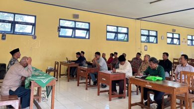 Foto sekelompok pria yang sedang serius mengikuti pelatihan aplikasi SatuMu MASA di dalam sebuah ruang kelas dengan bangku kayu dan dinding kuning. Tampak narasumber di depan kelas sedang mengarahkan peserta yang sedang mengoperasikan laptop.