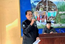Drs. Suyatmin Waskito Adi, M.Si, dari DKPTI UMS, sedang memberikan sambutan pada peluncuran Musuk IbuPreneur Village. Ia memegang mikrofon dan berdiri di depan spanduk acara.