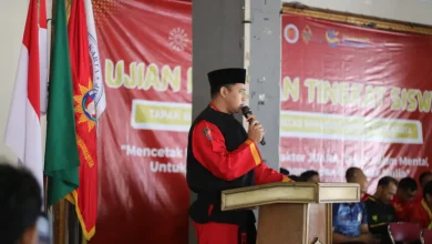 Sebuah gambar medium shot dari Dr. Eko Sudarmanto mengenakan seragam Tapak Suci berdiri di podium dan berbicara ke mikrofon.