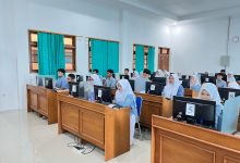Siswa-siswi SMA mengenakan seragam batik biru sedang fokus mengikuti ujian berbasis komputer atau ANBK di laboratorium komputer sekolah.