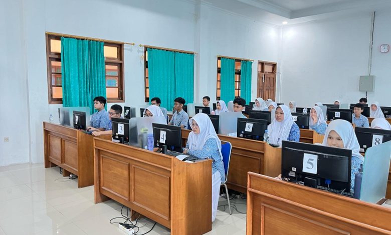 Siswa-siswi SMA mengenakan seragam batik biru sedang fokus mengikuti ujian berbasis komputer atau ANBK di laboratorium komputer sekolah.