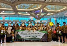 Sekelompok jamaah umroh dari KBIHU Ar-Roudloh Temanggung yang mengenakan batik identitas sedang berfoto bersama di terminal keberangkatan Bandara Yogyakarta International Airport (YIA), memegang spanduk pelepasan tanggal 22 Juni 2026.