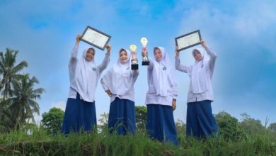 Empat santriwati MTs Almatera Temanggung berpose memegang dua piala dan dua sertifikat penghargaan TKA nasional di area persawahan di bawah langit biru.