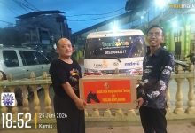 Dua pria berpose di depan ambulans memegang kotak donasi bertuliskan: "Sepatu untuk Masyarakat Aceh Tamiang dari Panglima Korps Marinir". Di latar belakang terdapat bangunan, pagar kuning, dan logo "bankziska", "lazismu", "mdmc". Stempel waktu dan lokasi tertulis: "18:52 25 Juni 2026, Kota Kuala Simpang, Kabupaten Aceh Tamiang".