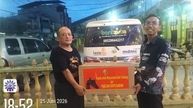 Dua pria berpose di depan ambulans memegang kotak donasi bertuliskan: "Sepatu untuk Masyarakat Aceh Tamiang dari Panglima Korps Marinir". Di latar belakang terdapat bangunan, pagar kuning, dan logo "bankziska", "lazismu", "mdmc". Stempel waktu dan lokasi tertulis: "18:52 25 Juni 2026, Kota Kuala Simpang, Kabupaten Aceh Tamiang".