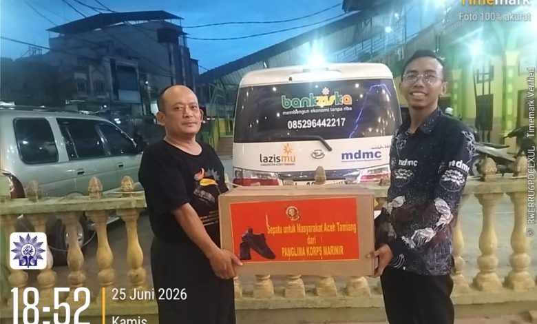Dua pria berpose di depan ambulans memegang kotak donasi bertuliskan: "Sepatu untuk Masyarakat Aceh Tamiang dari Panglima Korps Marinir". Di latar belakang terdapat bangunan, pagar kuning, dan logo "bankziska", "lazismu", "mdmc". Stempel waktu dan lokasi tertulis: "18:52 25 Juni 2026, Kota Kuala Simpang, Kabupaten Aceh Tamiang".