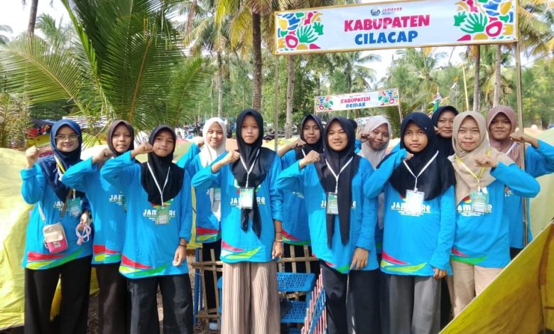 Sekelompok siswi berhijab berpose di depan gerbang tenda "KABUPATEN CILACAP" saat Jambore di pantai.