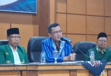 Pembicara utama mengenakan kemeja lurik biru sedang berbicara menggunakan mikrofon dalam rapat kerja pengembangan pendidikan Muhammadiyah Magelang.