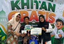 Seorang anak peserta khitan gratis didampingi pendamping dan panitia menunjukkan sertifikat di depan backdrop kegiatan Lazismu dan RS PKU Muhammadiyah Sukoharjo.