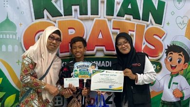 Seorang anak peserta khitan gratis didampingi pendamping dan panitia menunjukkan sertifikat di depan backdrop kegiatan Lazismu dan RS PKU Muhammadiyah Sukoharjo.