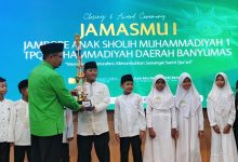 Santri TPQ Nur Hidayah Tanjung berpose bangga dengan piala Juara Umum di panggung Closing Ceremony JamasMu I Banyumas, bersama pembina dan latar belakang layar LED besar.