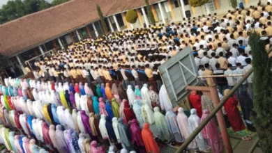 Ratusan siswa-siswi sekolah berkumpul dan berbaris rapi di lapangan untuk melakukan sholat dhuha berjamaah di masjid sekolah, terlihat siswa laki-laki di depan dengan seragam pramuka dan siswa perempuan di belakang dengan mukena warna-warni.