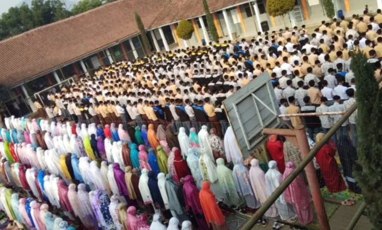Ratusan siswa-siswi sekolah berkumpul dan berbaris rapi di lapangan untuk melakukan sholat dhuha berjamaah di masjid sekolah, terlihat siswa laki-laki di depan dengan seragam pramuka dan siswa perempuan di belakang dengan mukena warna-warni.