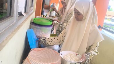 Dua peserta didik mengenakan jilbab dan seragam bermotif sedang mengambil makanan dalam suasana prasmanan.