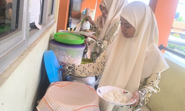 Dua peserta didik mengenakan jilbab dan seragam bermotif sedang mengambil makanan dalam suasana prasmanan.