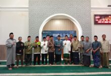 Sekelompok pria mengenakan baju koko dan sarung berfoto bersama dengan gaya jempol di depan spanduk acara Kuliah Subuh.